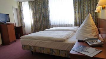 A hotel room with two beds, a desk with a lamp, a telephone, and a television.