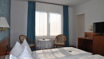 A hotel room with a bed, two chairs, a small table, a TV, and a desk.