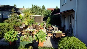 Un patio al aire libre con varias mesas y sillas, rodeado de plantas en macetas y follaje.