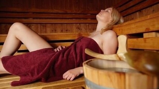 Una persona en una cabaña de sauna de madera con bancos y un balde de madera.