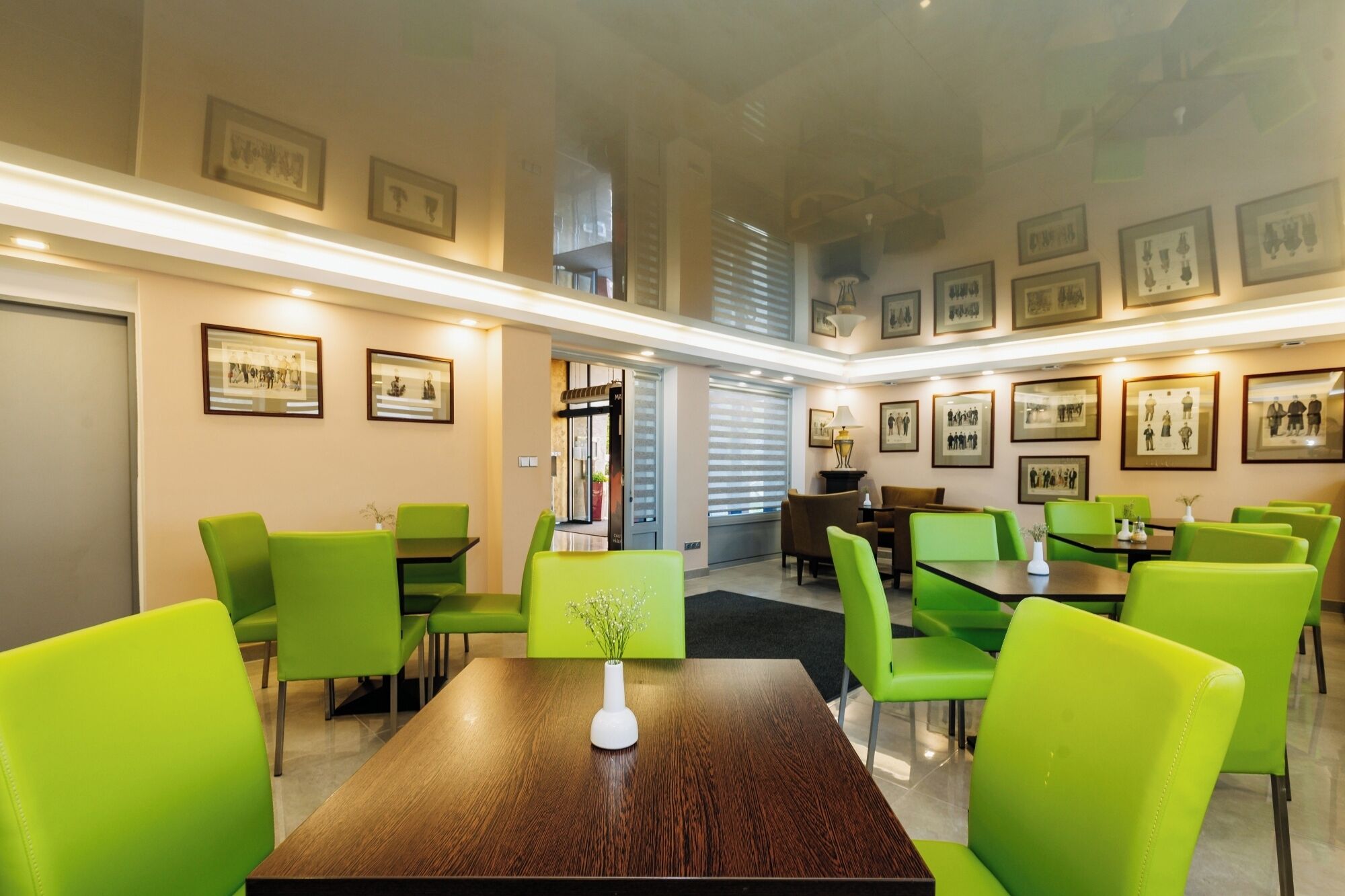 Un espace de restauration moderne avec des chaises vertes et des tables en bois, des tableaux encadrés aux murs et un escalier en arrière-plan.