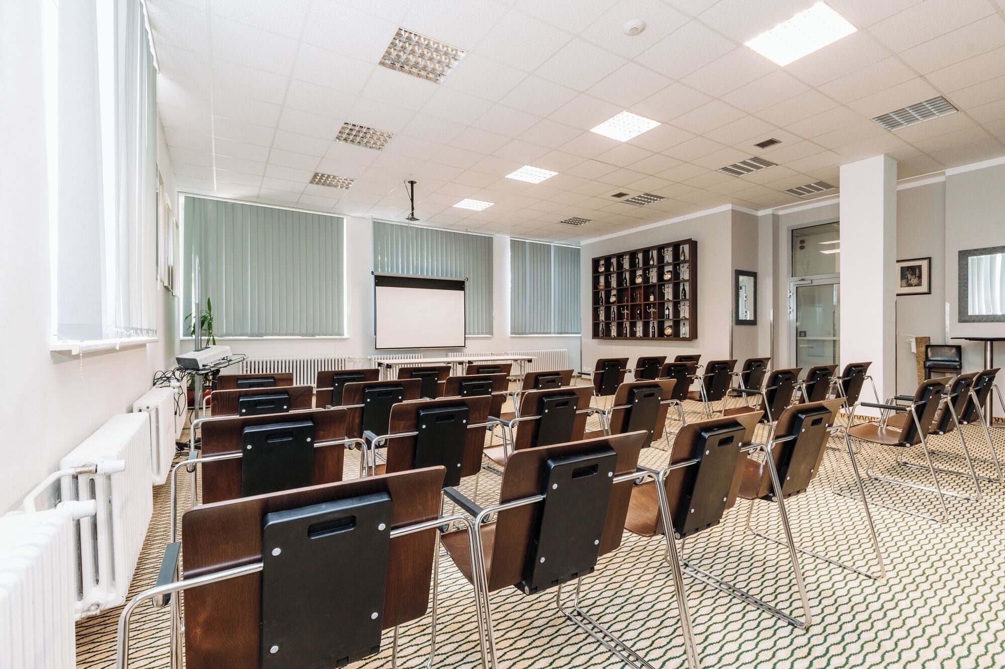 Une salle de conférence avec des rangées de chaises, un écran de projection et une bibliothèque contenant divers objets.