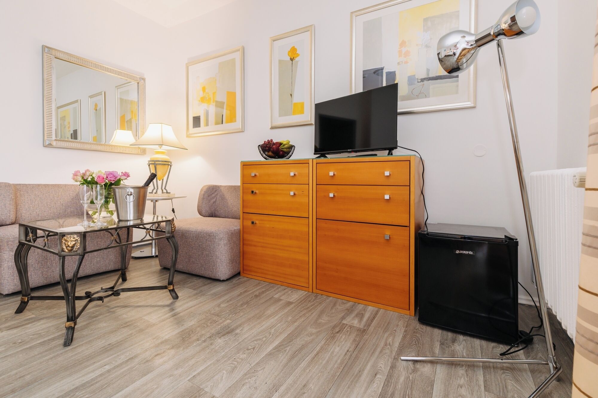 A modern living room with a sofa, a coffee table, a lamp, a TV, a wooden cabinet, and a radiator.