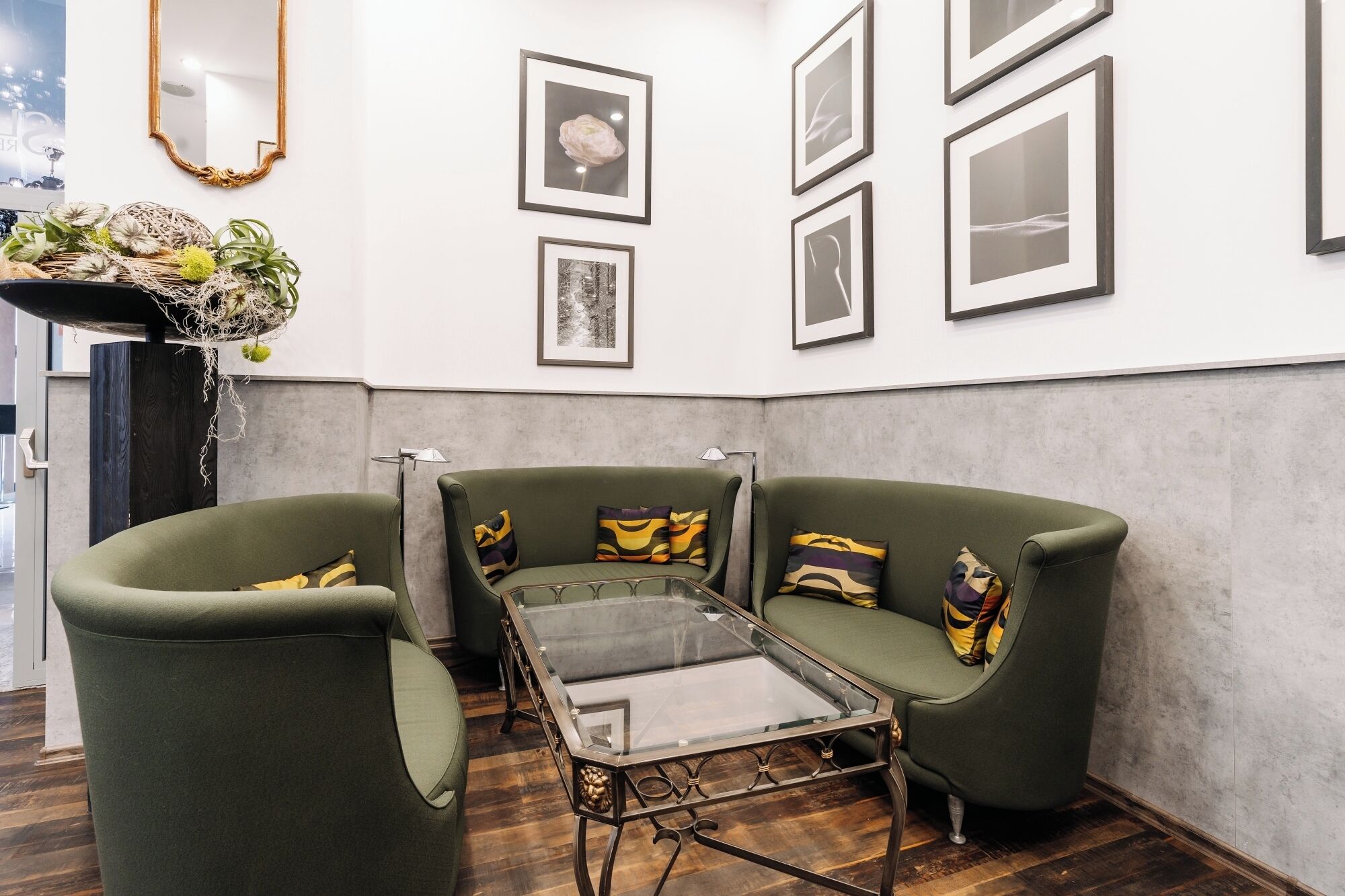 A modern living room with a glass coffee table, two green armchairs, and a sofa.