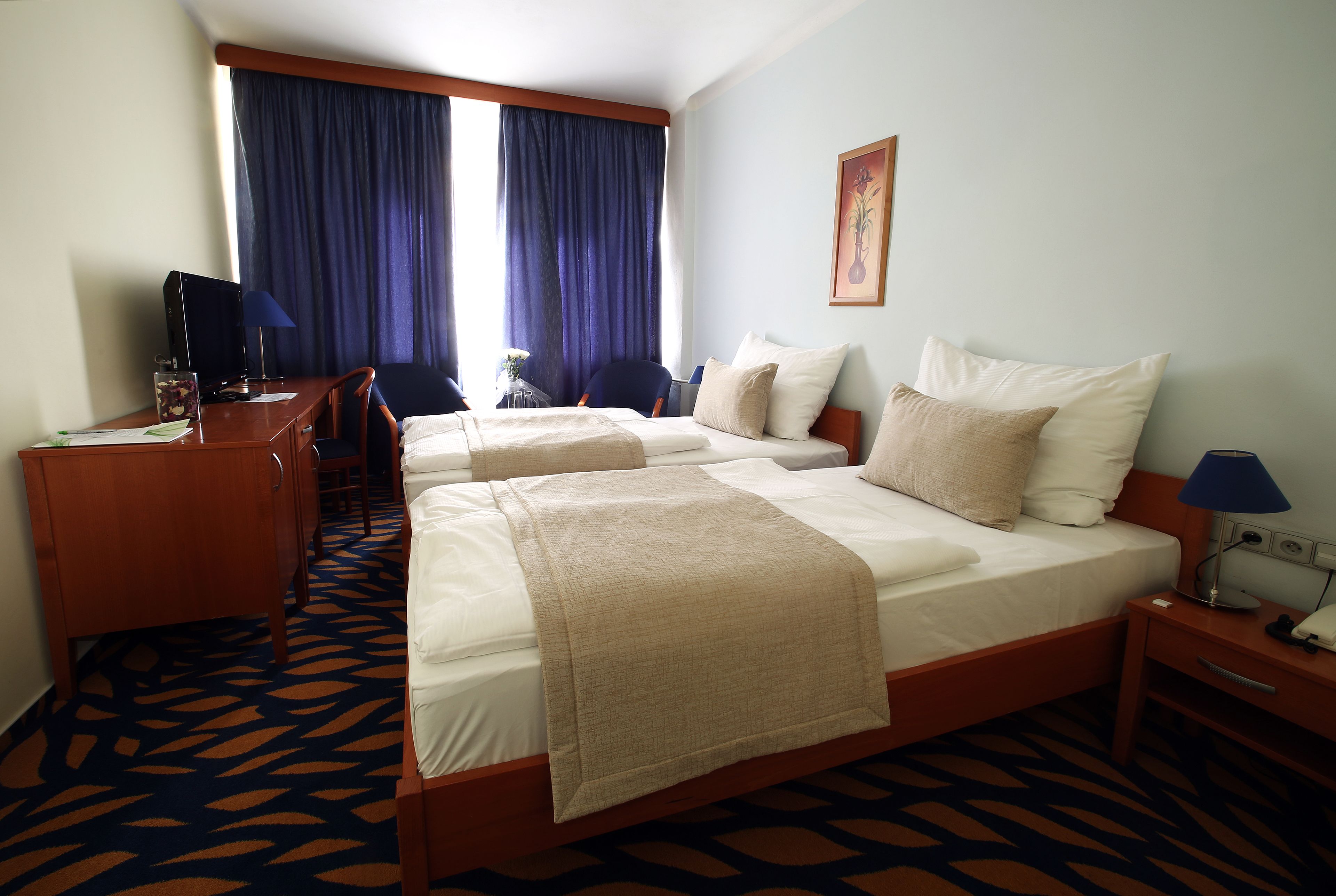 A hotel room with two beds, a desk, a chair, a lamp, and a window with curtains.