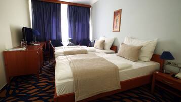 A hotel room with two beds, a desk, a chair, a lamp, and a window with curtains.