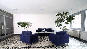 A modern living room with a patterned floor, two blue armchairs, a coffee table, and two potted plants. - Central Hotel Pilsen (Plzen)