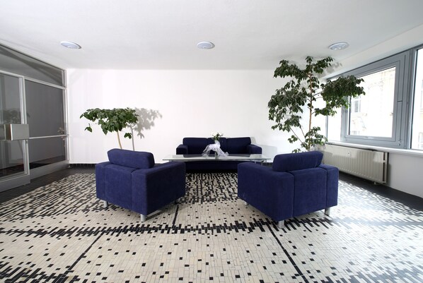 Ein modernes Wohnzimmer mit einem gemusterten Boden, zwei blauen Sesseln, einem Couchtisch und zwei Topfpflanzen.