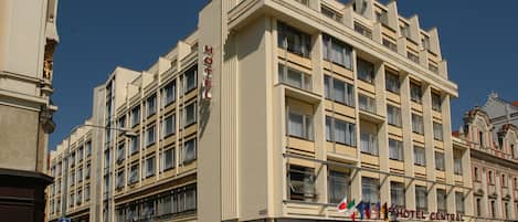 Un hotel de varios pisos con una entrada central, balcones y una exhibición de banderas.