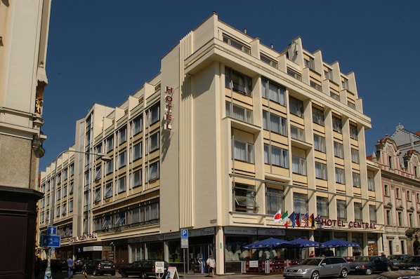 Un hotel de varios pisos con una entrada central, balcones y una exhibición de banderas.