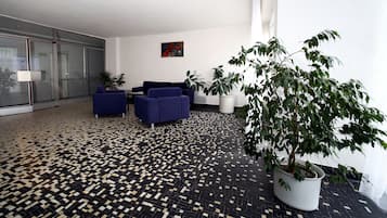 Um espaço interior moderno com piso estampado, dois sofás azuis, uma planta em vaso e um quadro na parede.