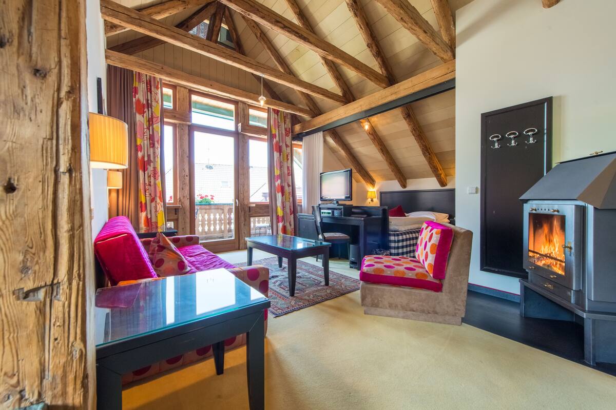 A cozy living room with a wooden ceiling, a fireplace, a television, and a sofa with colorful cushions.