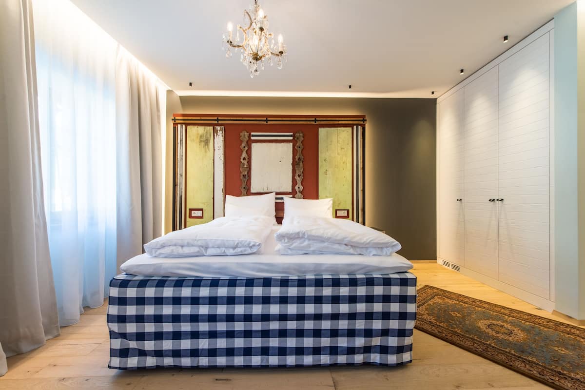 A bedroom with a large bed, a chandelier, a wardrobe, and a patterned rug.