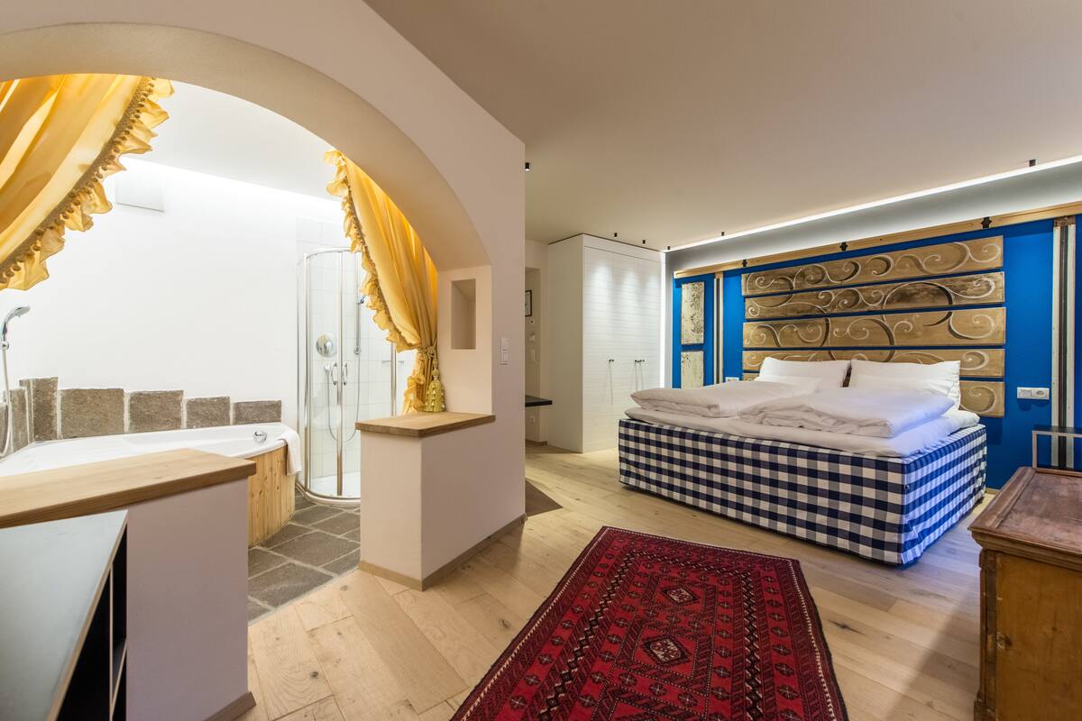 A bedroom with a checkered bed, a red rug, and a blue headboard.