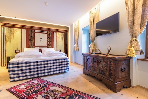 A bedroom with a checkered bed, a wooden dresser, a flat-screen TV, and a patterned rug.