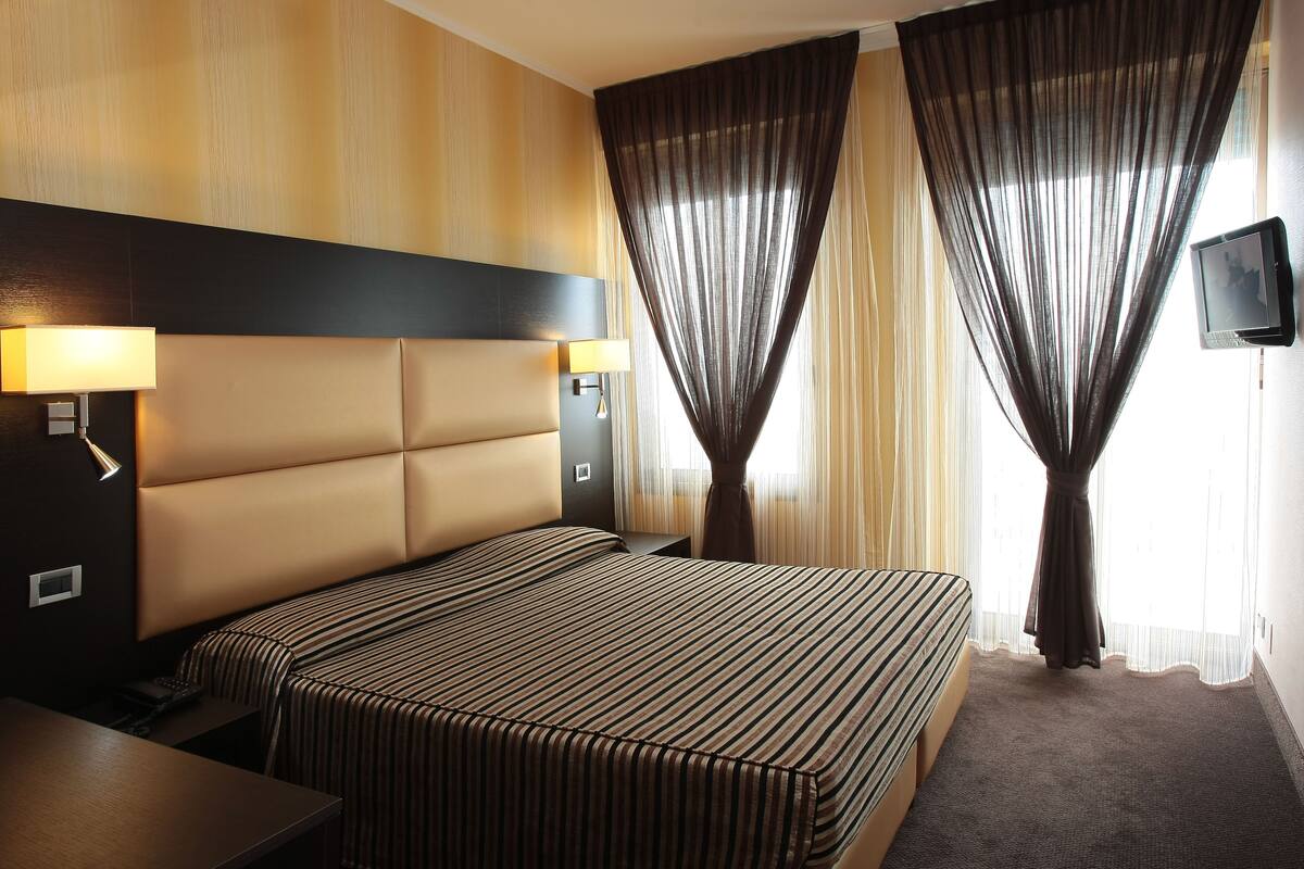 Une chambre d’hôtel avec un grand lit, des tables de chevet, une télévision et des rideaux.