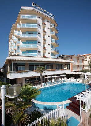 A hotel with a swimming pool, multiple balconies, and outdoor seating areas. - Hotel Rivamare (Jesolo)