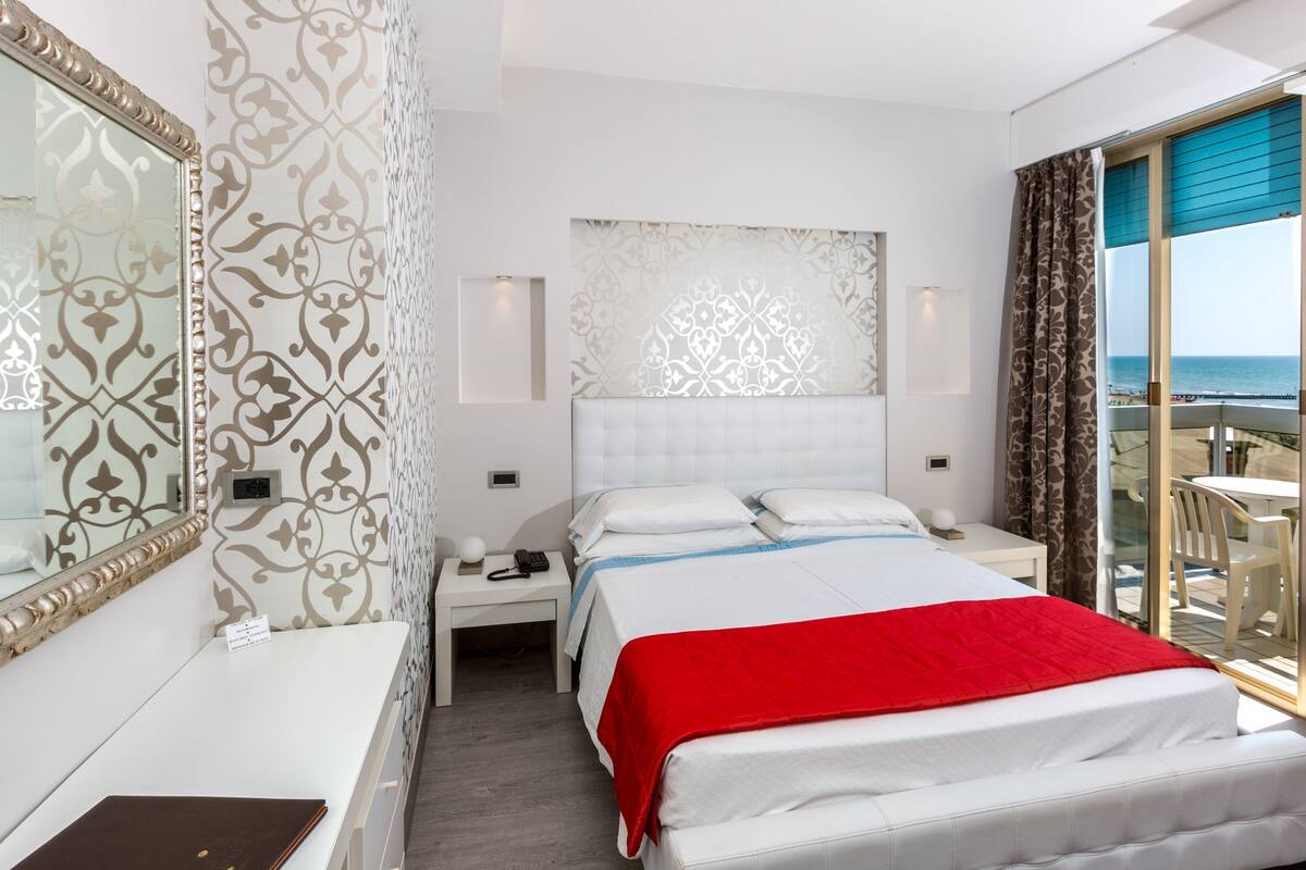 Une chambre d’hôtel avec un grand lit, une table de chevet, un miroir et une vue sur la plage.