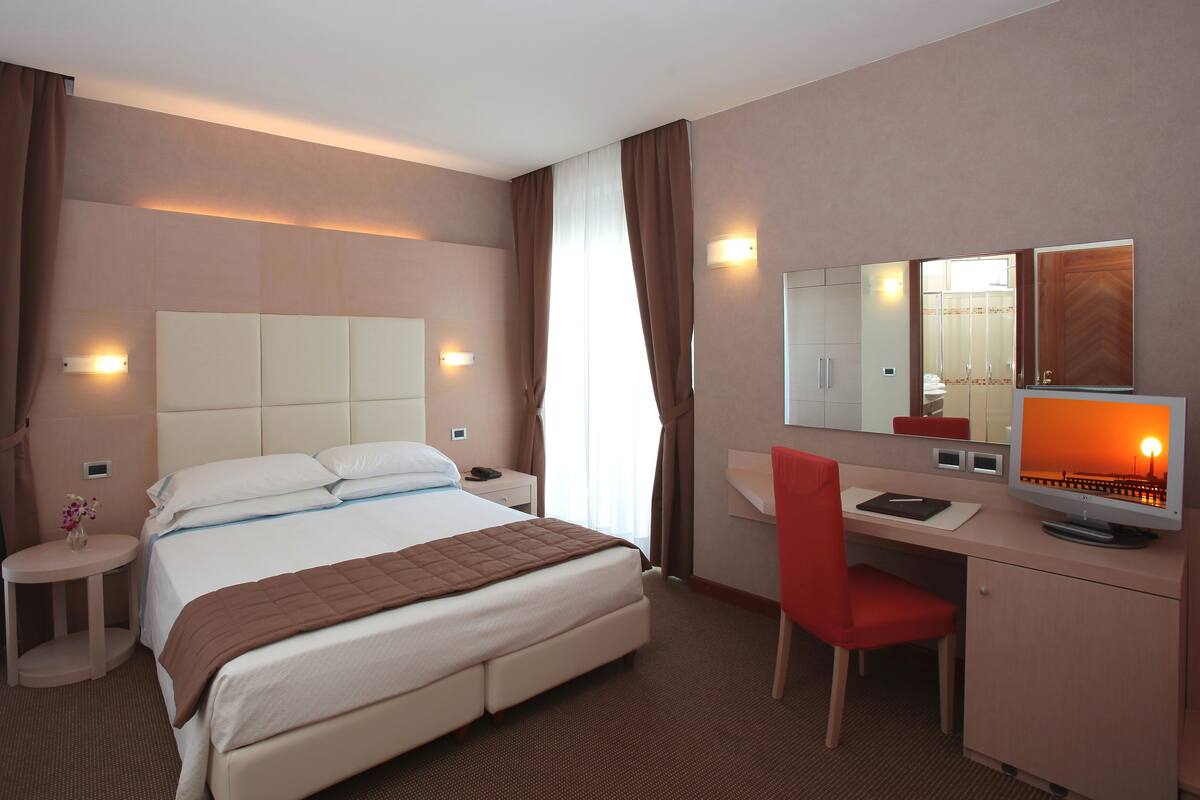 Une chambre d’hôtel comprenant un lit, un bureau avec une chaise, une table de chevet, un miroir et un téléviseur.