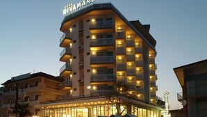 A multi-story hotel with balconies, a prominent sign, and a well-lit facade. - Hotel Rivamare (Jesolo)