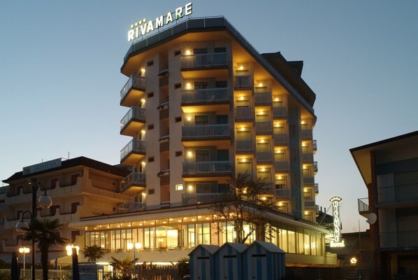 A multi-story hotel with balconies, a prominent sign, and a well-lit facade. - Hotel Rivamare (Jesolo)