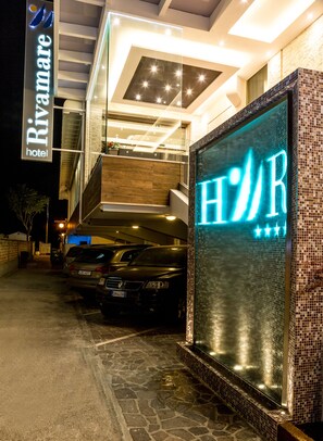 L’entrée d’un hôtel, avec une enseigne lumineuse au néon, un espace de stationnement couvert et une façade de bâtiment moderne.