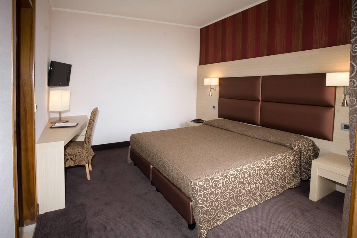 Une chambre d’hôtel équipée d’un lit, d’un bureau, d’une chaise, d’une télévision et de deux lampes de chevet.