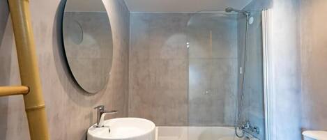 Un baño moderno con un espejo redondo, un lavabo blanco, una bañera y un inodoro.