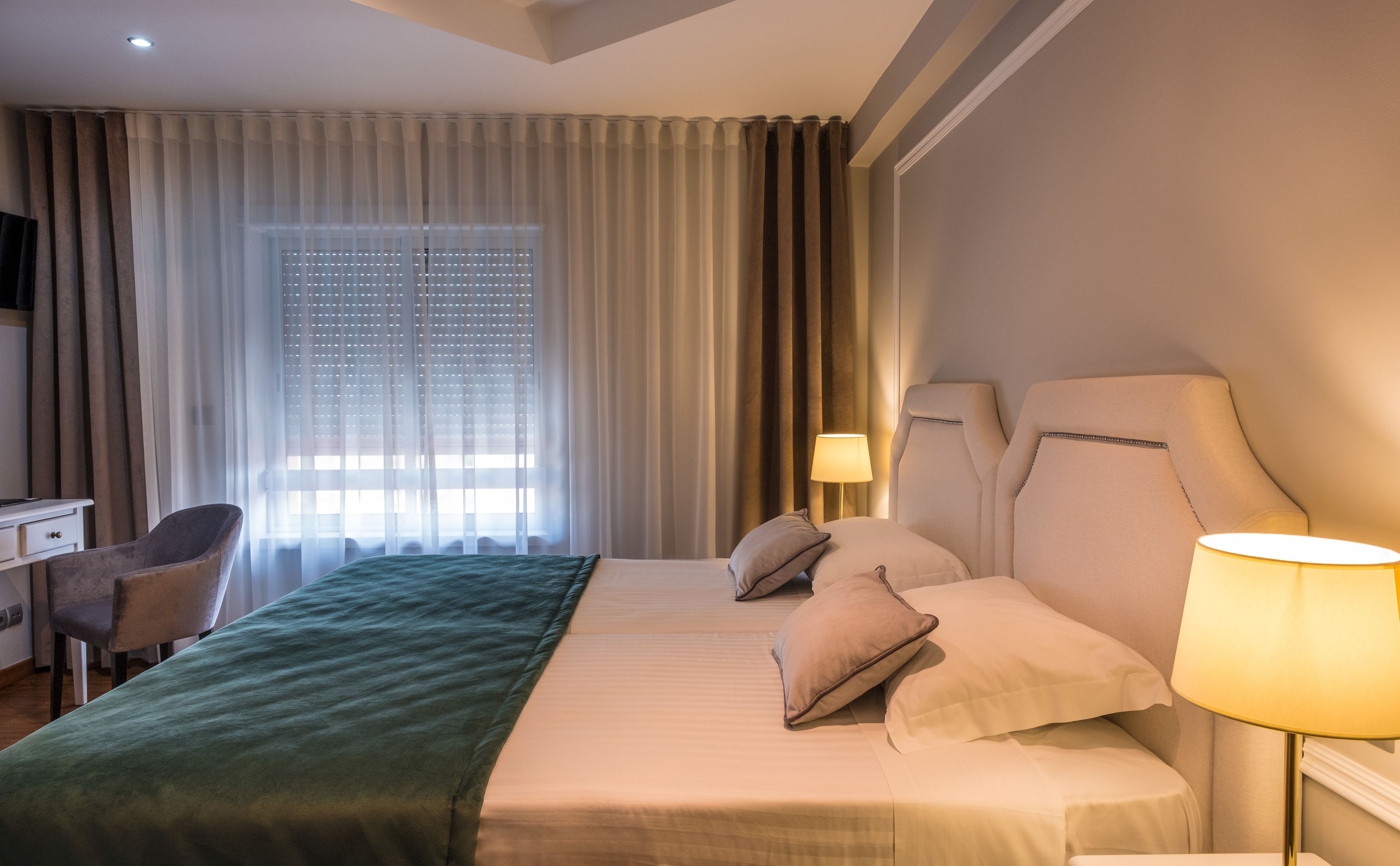 A hotel room with a bed, two bedside lamps, a desk, and a chair.