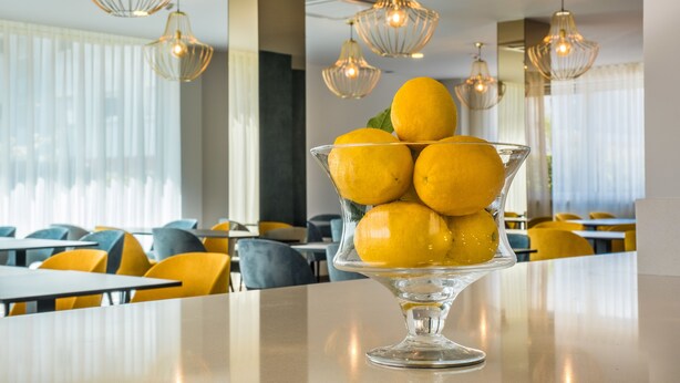 A dining area with a glass bowl of lemons on a table, yellow chairs, and hanging pendant lights. - Imperhotel by Umbral (Ourem)