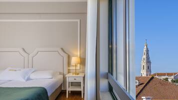 A hotel room with a bed, a nightstand with a lamp, and a window with a view of a tower.