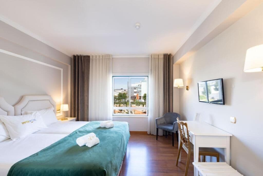 Een hotelkamer met twee bedden, een bureau, een stoel, een raam met uitzicht en een televisie aan de muur.