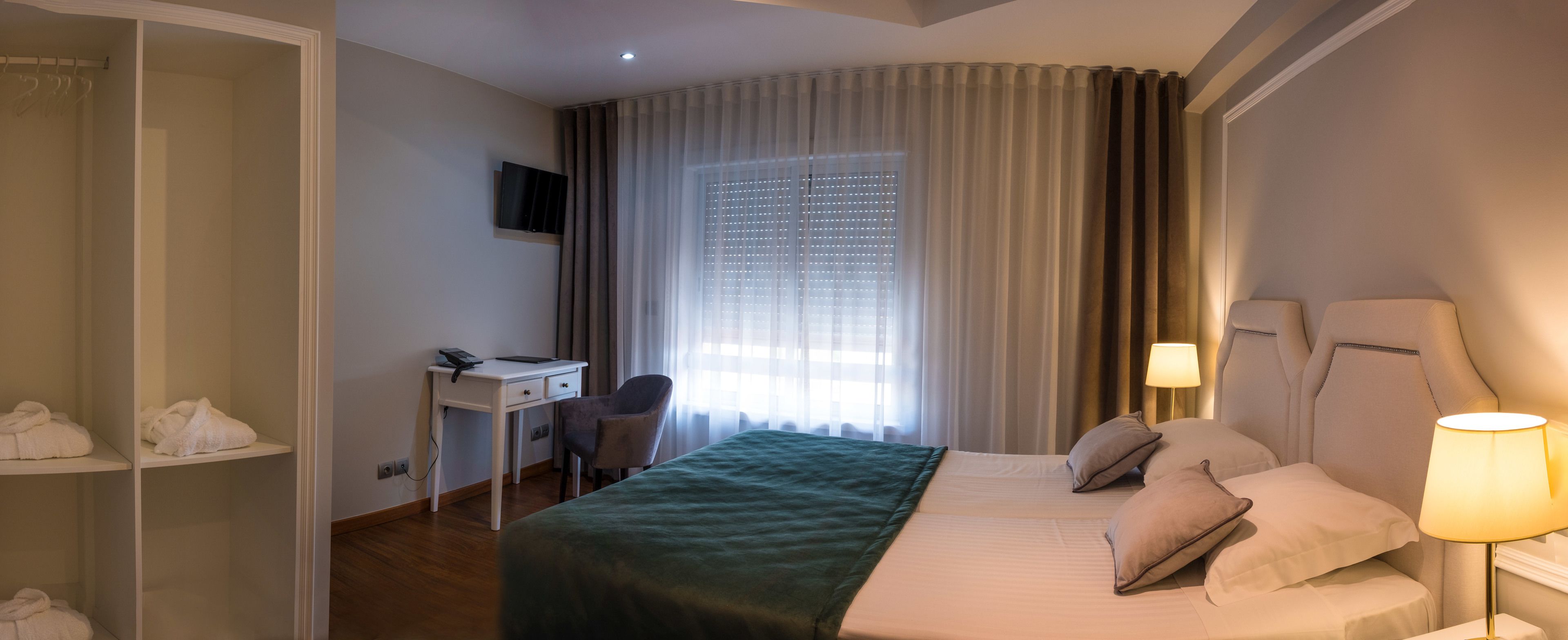 Een hotelkamer met een bed, een bureau, een stoel, een televisie en een kast.
