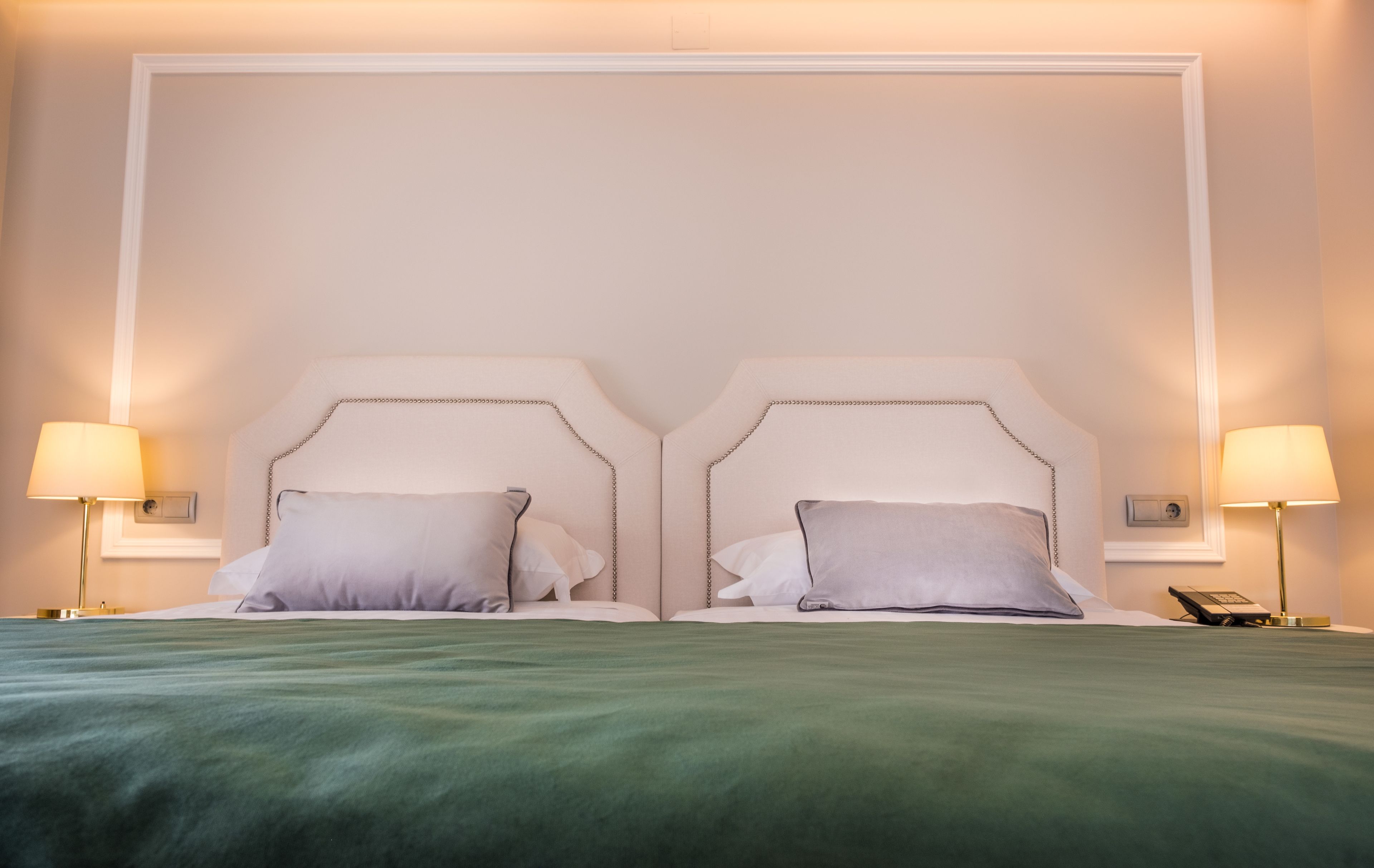 Una cama doble con una colcha verde, dos lámparas de noche y un teléfono en la mesita de noche.