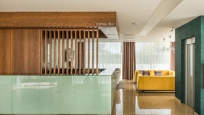 A modern reception area with a glass counter, a coffee bar, a yellow sofa, and a green armchair. - Imperhotel by Umbral (Ourem)