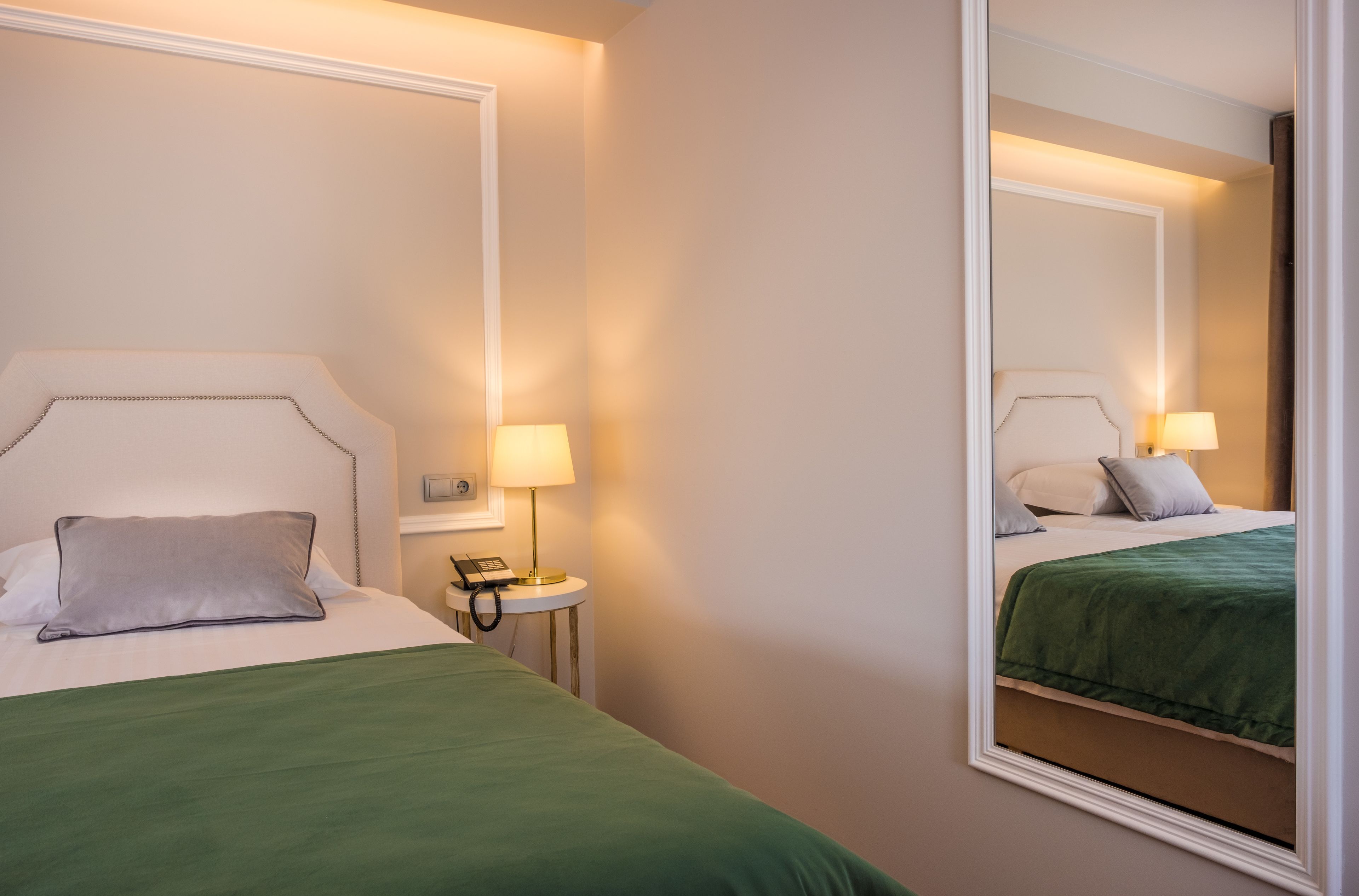 Ein Hotelzimmer mit Bett, Nachttisch, Lampe und Spiegel.