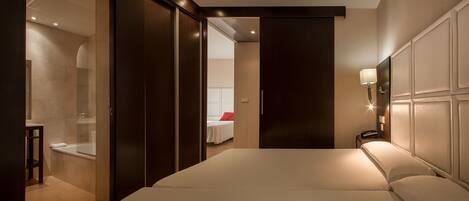 A modern hotel room with a large bed, a separate bathroom with a glass shower enclosure, and a bedside table.