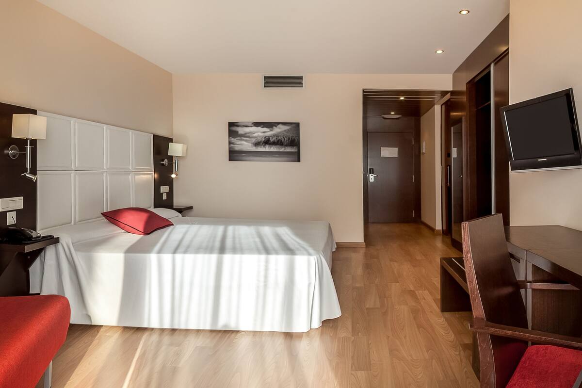 Ein Hotelzimmer mit Bett, Schreibtisch, Fernseher und einem roten Sessel.