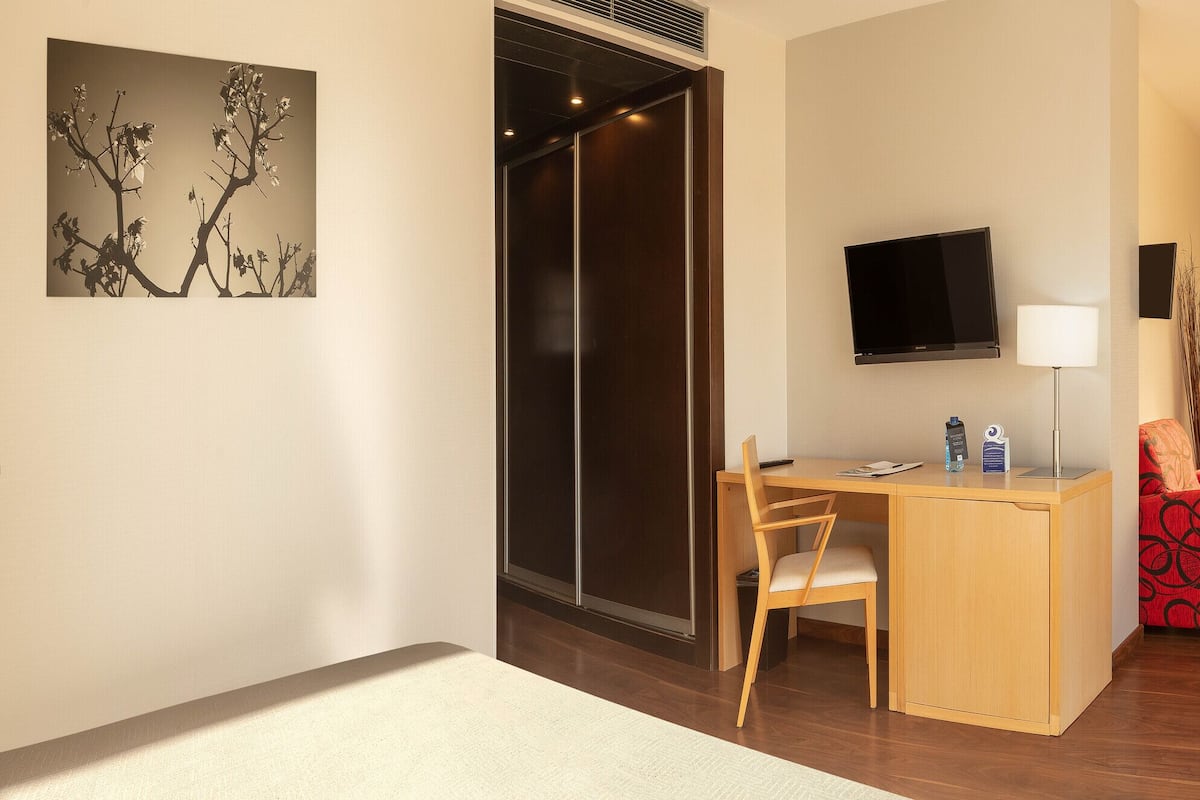 Ein Hotelzimmer mit Schreibtisch, Stuhl, Bett und einem Balkon mit Sitzgelegenheiten.