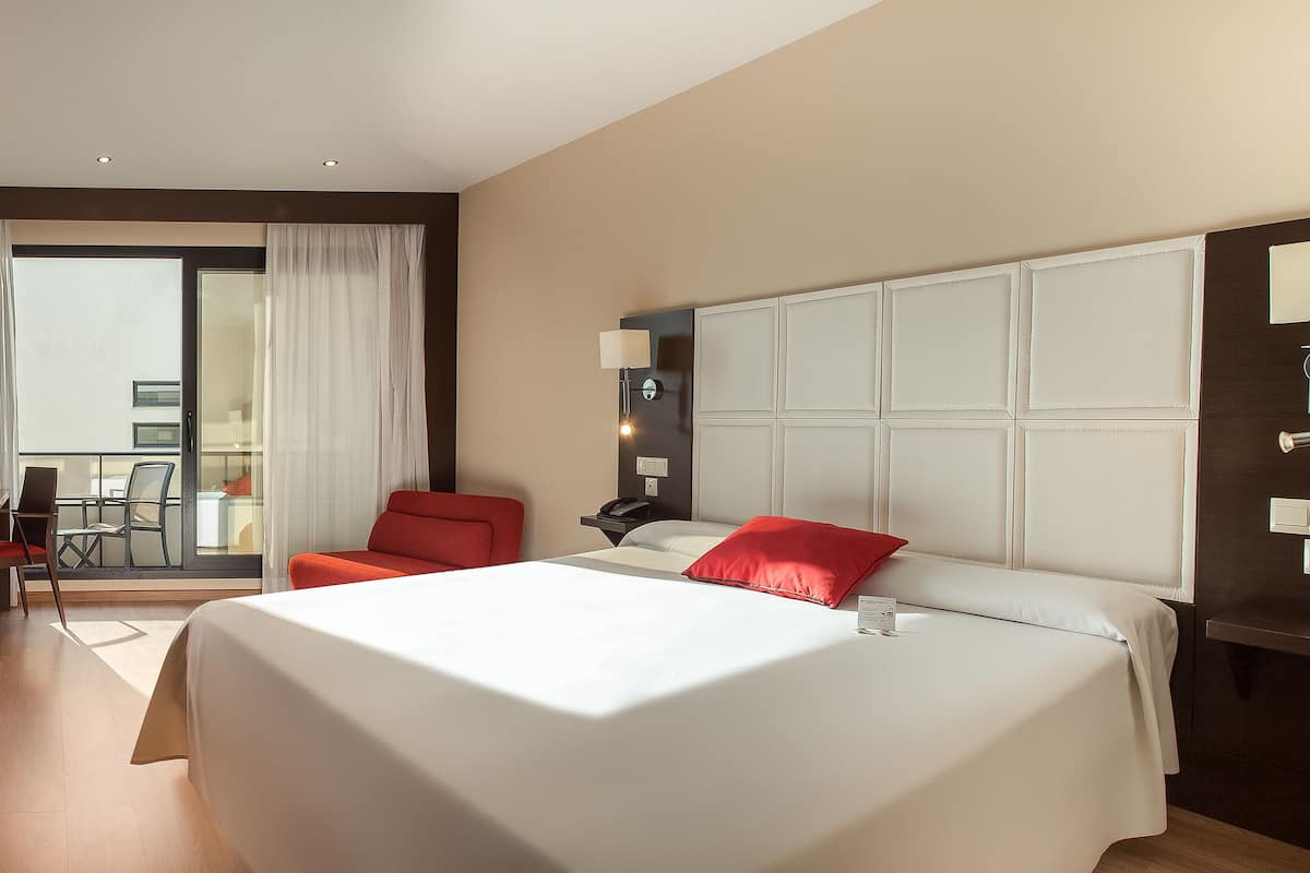 Ein Hotelzimmer mit einem großen Bett, einem Schreibtisch mit Stuhl, einem Fernseher und einem Balkon mit Blick.