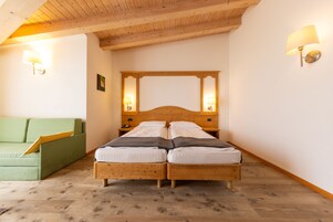 A bedroom with a wooden bed, two bedside lamps, a green sofa, and a wooden ceiling.
