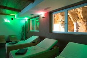 Un cuarto de spa con tumbonas de madera, un ventanal con vista a rocas e iluminación ambiental verde.