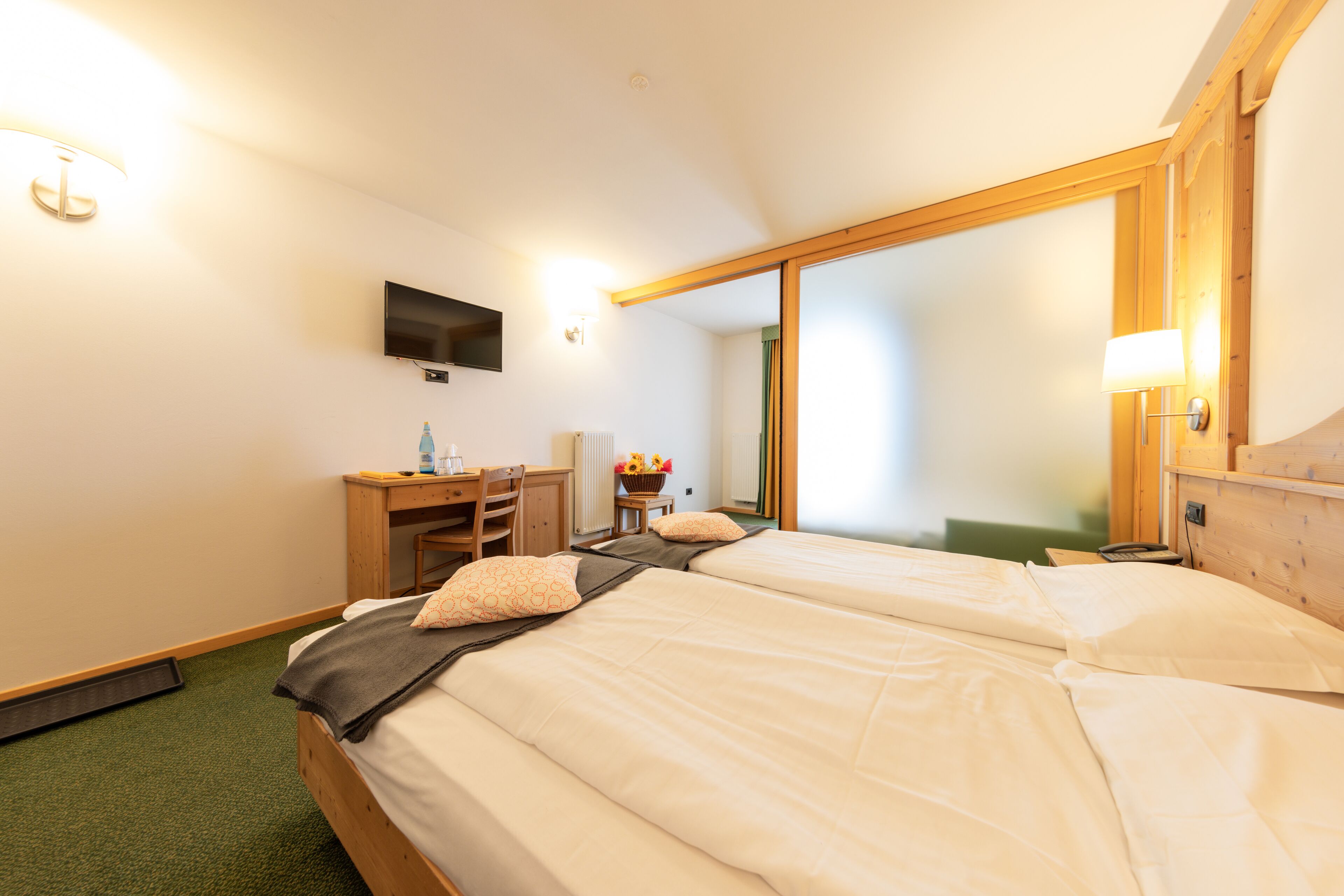 A hotel room with two beds, a desk, a chair, a TV, and a large mirror.