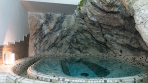 Un jacuzzi con piso de mosaicos y pared de roca de fondo.