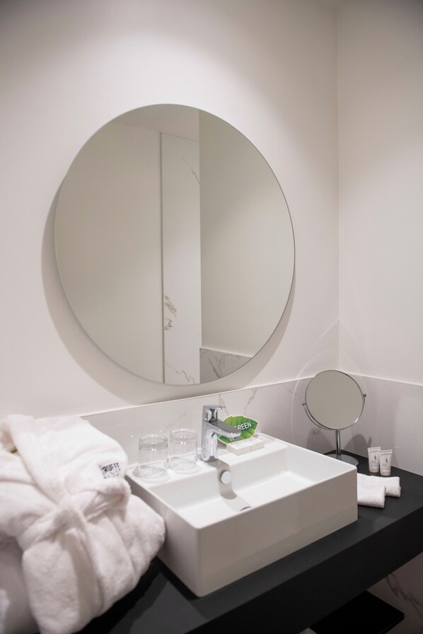 A modern bathroom with a large round mirror, a white sink, and a black countertop.
