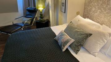 Un dormitorio con una cama, almohadas, una silla, una lámpara y un papel tapiz con diseño.