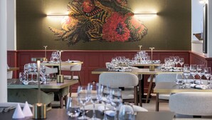 Un restaurante con mesas dispuestas para comer, un cuadro abstracto grande en la pared y una iluminación cálida.