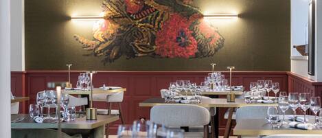 Un restaurante con mesas dispuestas para comer, un cuadro abstracto grande en la pared y una iluminación cálida.