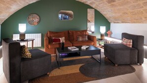 Un salón acogedor con techo de piedra, pared verde decorativa y sofá marrón.