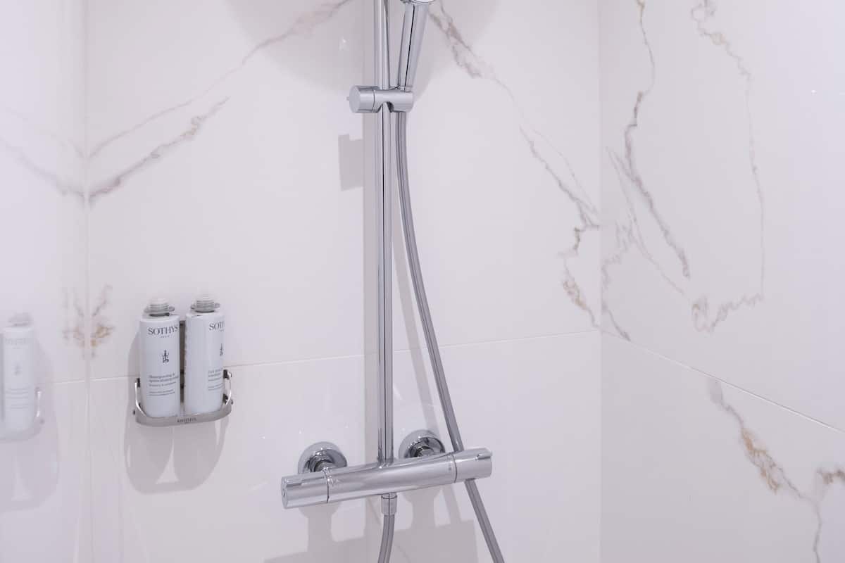 A shower with a handheld showerhead and a wall-mounted control.